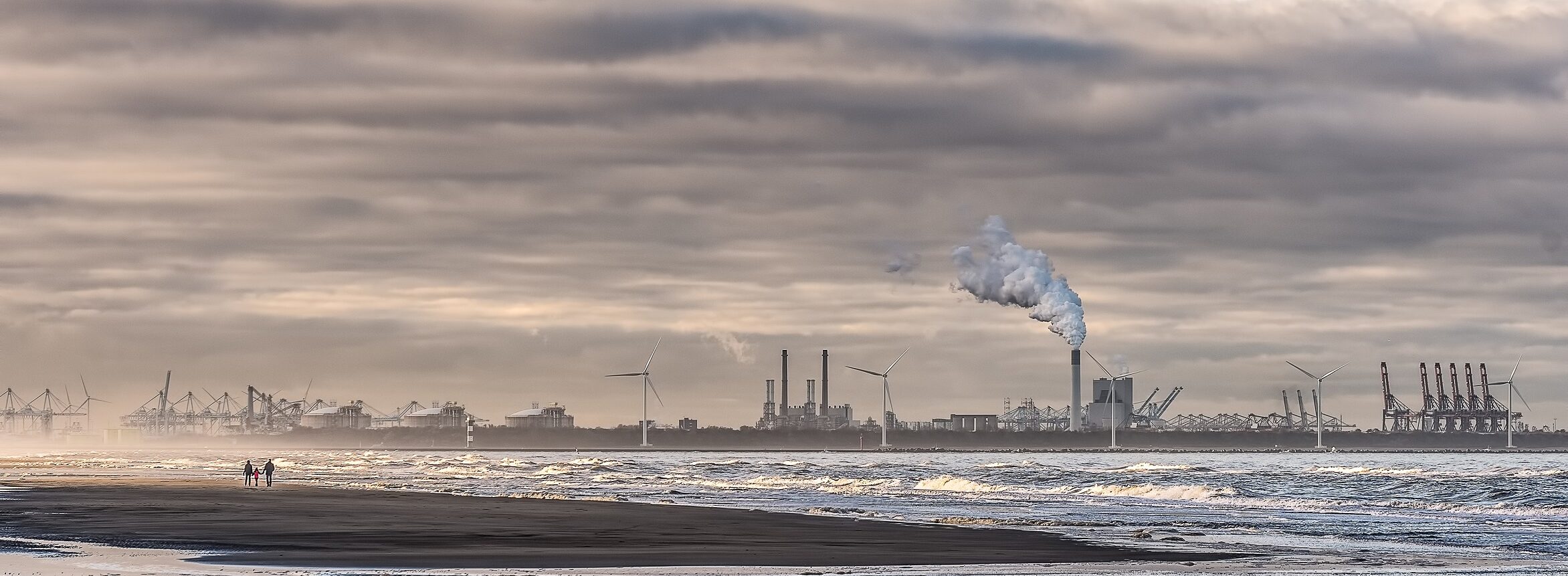 shot of a sea with windmills and factory in the distance under a cloudy sky